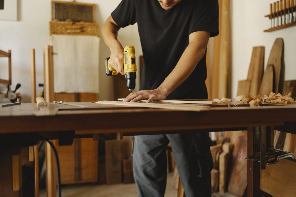 Crop carpenter drilling wooden plank in workshop